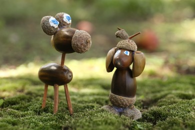 Cute figures made of acorns on green moss outdoors, closeup