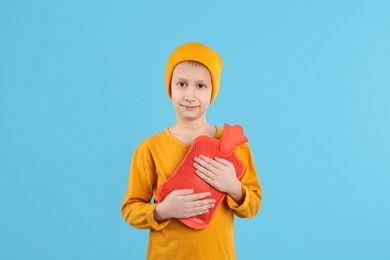 Ill boy with hot water bottle suffering from cold on light blue background