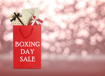 Red shopping bag with text Boxing Day Sale full of gifts on blurred pink background, closeup. Space for text