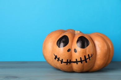 Pumpkin with drawn spooky face on light blue background, space for text. Halloween celebration