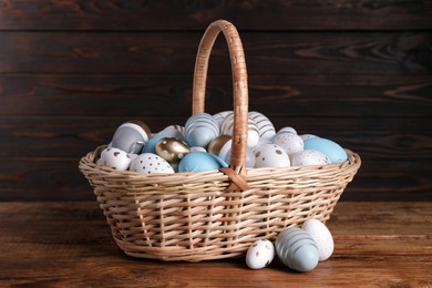 Photo of Wicker basket with festively decorated Easter eggs on wooden table
