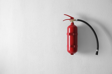 Fire extinguisher hanging on white wall. Space for text