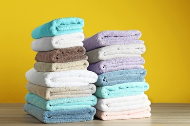 Different fresh soft terry towels on wooden table against yellow background