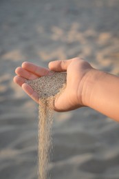 Photo of Girl pouring sand from hand outdoors, closeup. Fleeting time concept