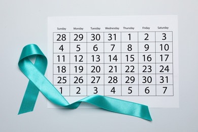 Teal awareness ribbon and calendar on white background, top view. Symbol of social and medical issues