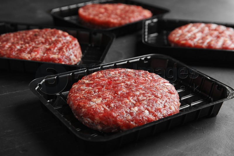Plastic containers with raw meat cutlets for burger on grey table, closeup