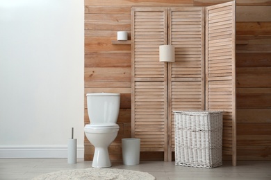 Toilet bowl near wooden wall in modern bathroom interior