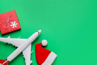 Santa hat, toy airplane, gift box and space for text on green background, flat lay. Christmas vacation