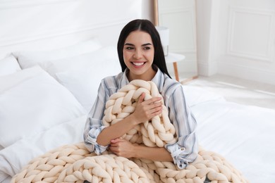 Young woman with chunky knit blanket on bed at home