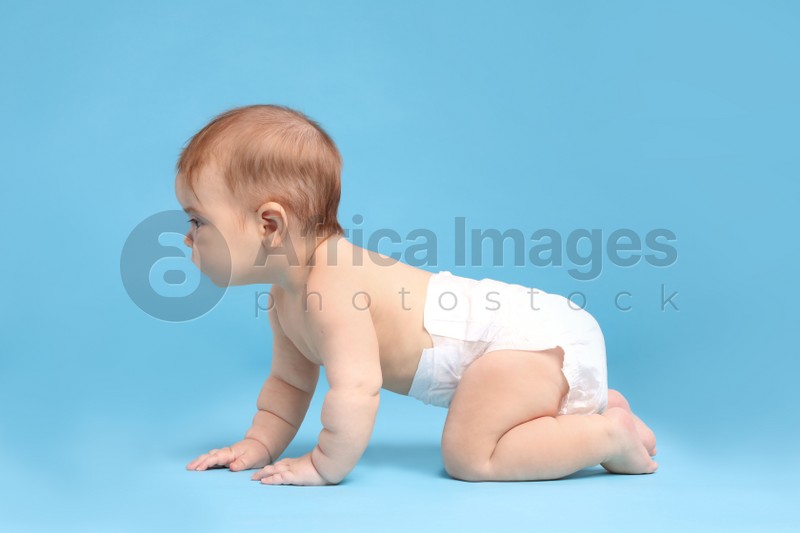 Cute little baby in diaper crawling on light blue background