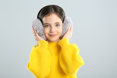 Cute girl wearing stylish earmuffs on grey background