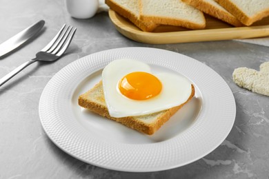 Photo of Heart shaped fried egg served on grey marble table