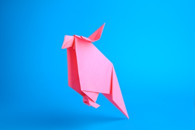 Photo of Origami art. Handmade pink paper parrot on light blue background