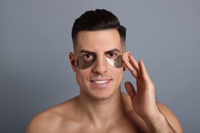 Man applying dark under eye patch on grey background