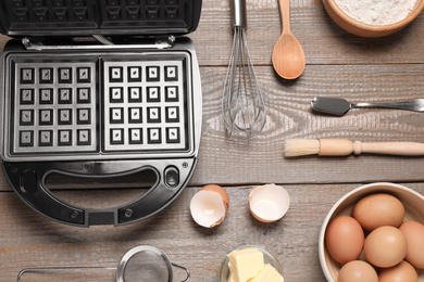Photo of Flat lay composition with ingredients and Belgian waffle maker on wooden table
