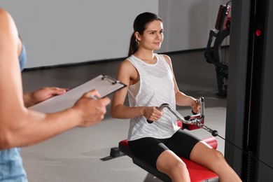 Photo of Woman doing exercise in modern gym while trainer looking at workout plan