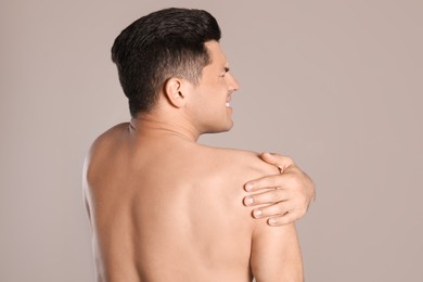 Man suffering from shoulder pain on beige background, back view