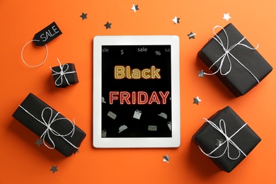Tablet with Black Friday announcement and gifts on orange background, flat lay