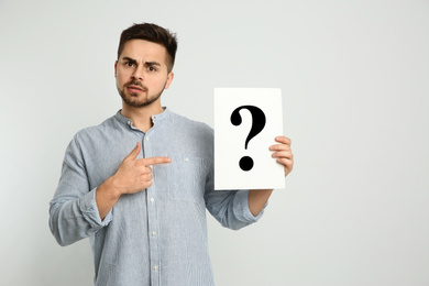 Photo of Confused man holding question mark sign on light background