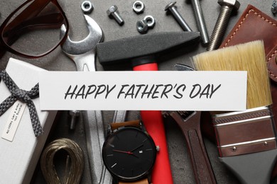 Card with phrase HAPPY FATHER'S DAY, different tools and male accessories on grey background, flat lay