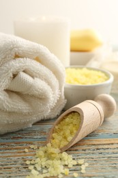 Photo of Wooden scoop of yellow sea salt and towel on rustic table, closeup