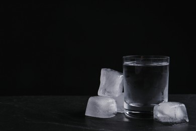 Vodka in shot glass with ice on table against black background. Space for text