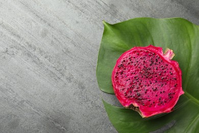 Delicious cut red pitahaya fruit and green leaf on grey table, flat lay. Space for text
