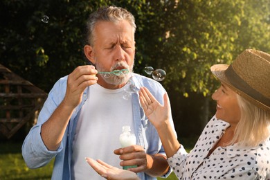 Photo of Lovely mature couple spending time together in park. Man blowing soap bubbles