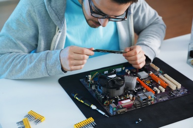 Photo of Male technician repairing computer motherboard at table