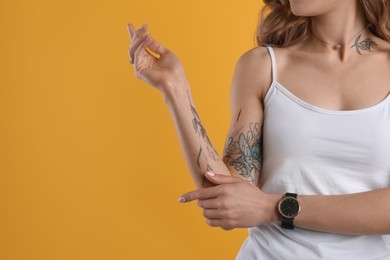 Photo of Beautiful woman with tattoos on body against yellow background, closeup. Space for text