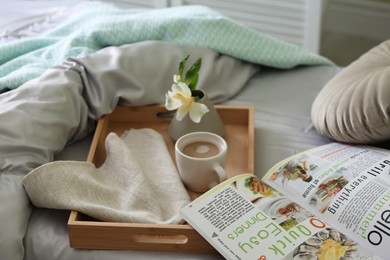 Cup of coffee, flower and magazine on bed with fresh linens indoors