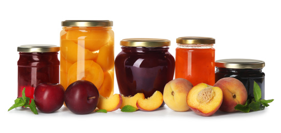 Glass jars with different pickled fruits and jam on white background
