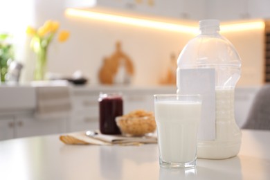 Gallon bottle of milk, glass and breakfast cereal on white table in kitchen. Space for text