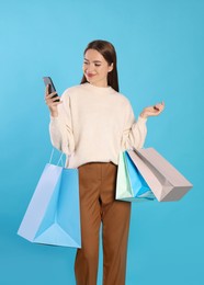 Happy young woman with shopping bags and smartphone on light blue background. Big sale