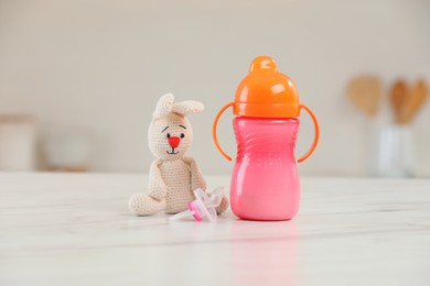 Baby bottle, toy and pacifier on white marble table indoors. Maternity leave concept