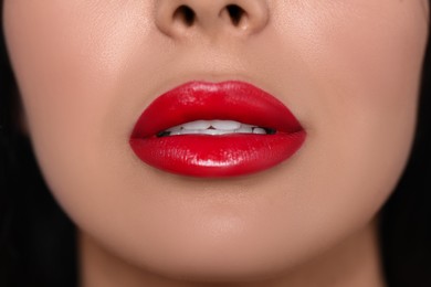 Photo of Young woman wearing beautiful red lipstick on dark background, closeup