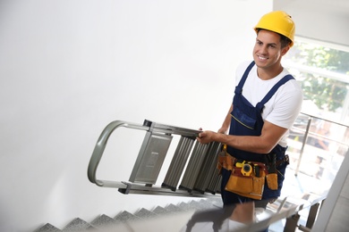 Professional builder carrying metal ladder up stairs