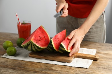 Woman cutting delicious watermelon at wooden table against light background, closeup