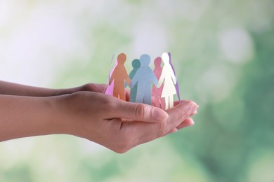 Photo of Woman holding paper human figures on blurred background, closeup. Diversity and Inclusion concept