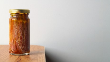 Photo of Jar with anchovy fillets in oil on wooden table. Space for text