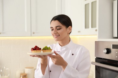 Happy professional confectioner with delicious tartlets in kitchen