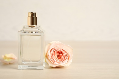 Bottle of perfume and beautiful rose on wooden table. Space for text