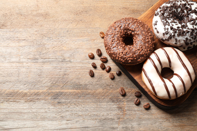 Yummy donuts with sprinkles on wooden table, flat lay. Space for text