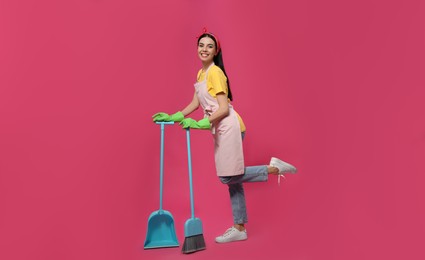 Photo of Young housewife with broom and scoop on pink background