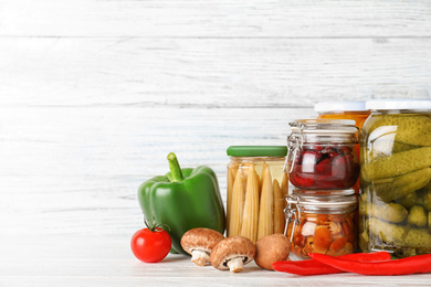 Glass jars with different pickled vegetables on white wooden table. Space for text