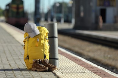 Photo of Yellow backpack, hiking boots and camping mat on railway platform outdoors. Tourism concept