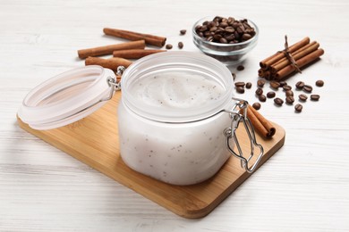 Body scrub in glass jar, cinnamon and coffee beans on white wooden table