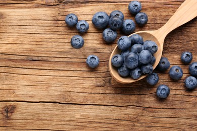 Spoon with tasty fresh blueberries on wooden table, flat lay. Space for text