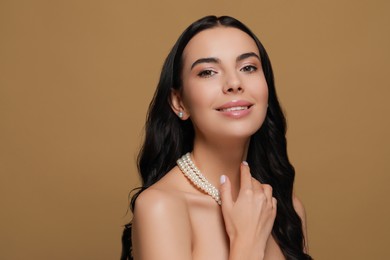 Photo of Young woman wearing elegant pearl jewelry on brown background, space for text