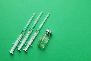Disposable syringes with needles and vial on green background, flat lay. Space for text